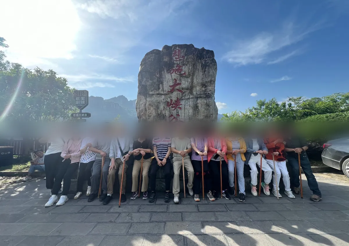 参团游客在恩施大峡谷石碑前合影,人人手持一根登山杖,背景为恩施大峡谷天然石碑
